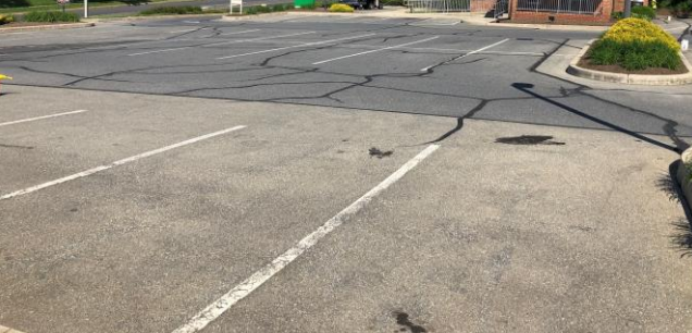 Old asphalt pavement, on a parking lot, that has turned grey. Also, there are black lines across it from being crack filled.